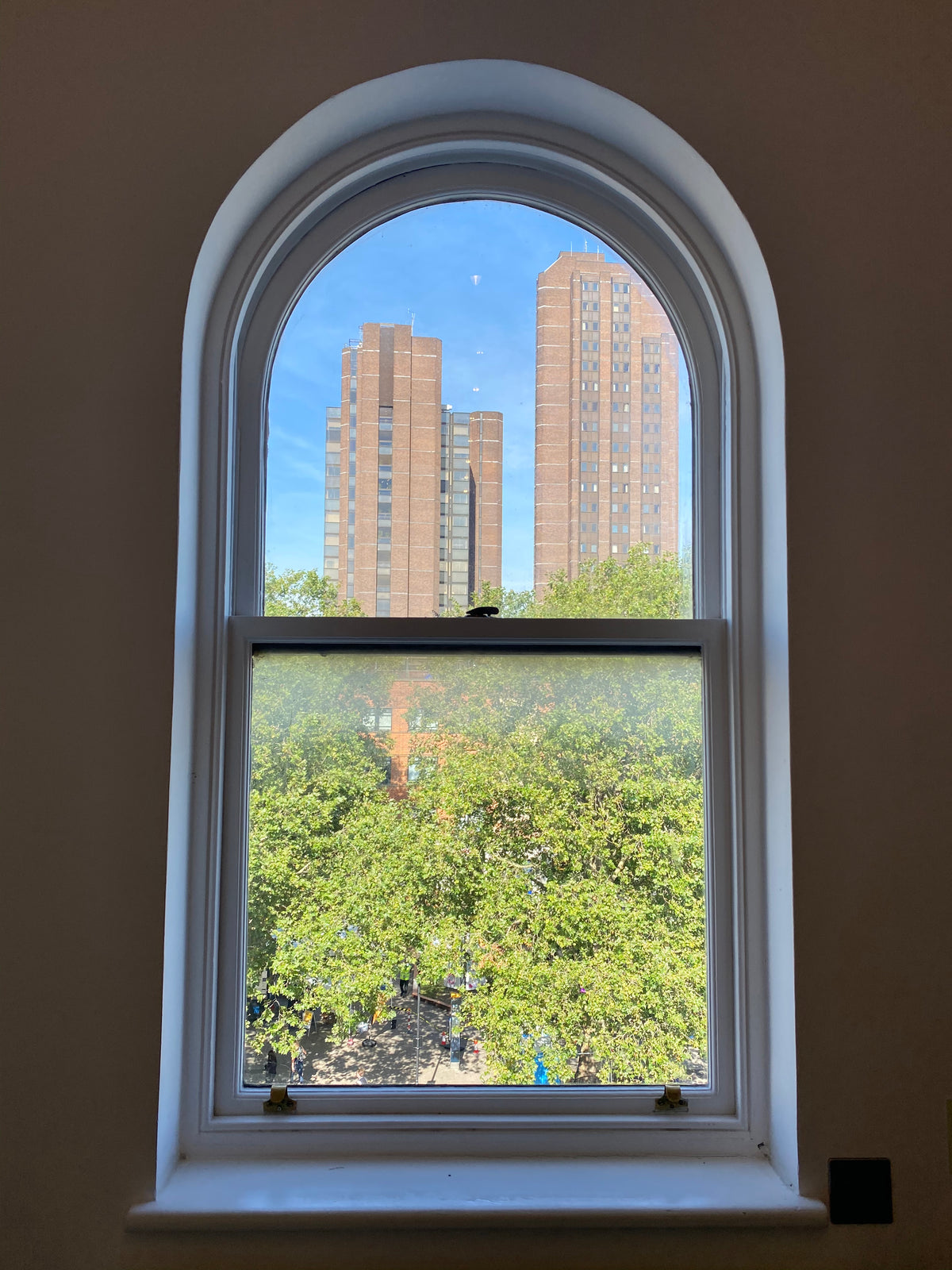 Arched window with view of trees and buildings with clear safety film applied for added safety and protection