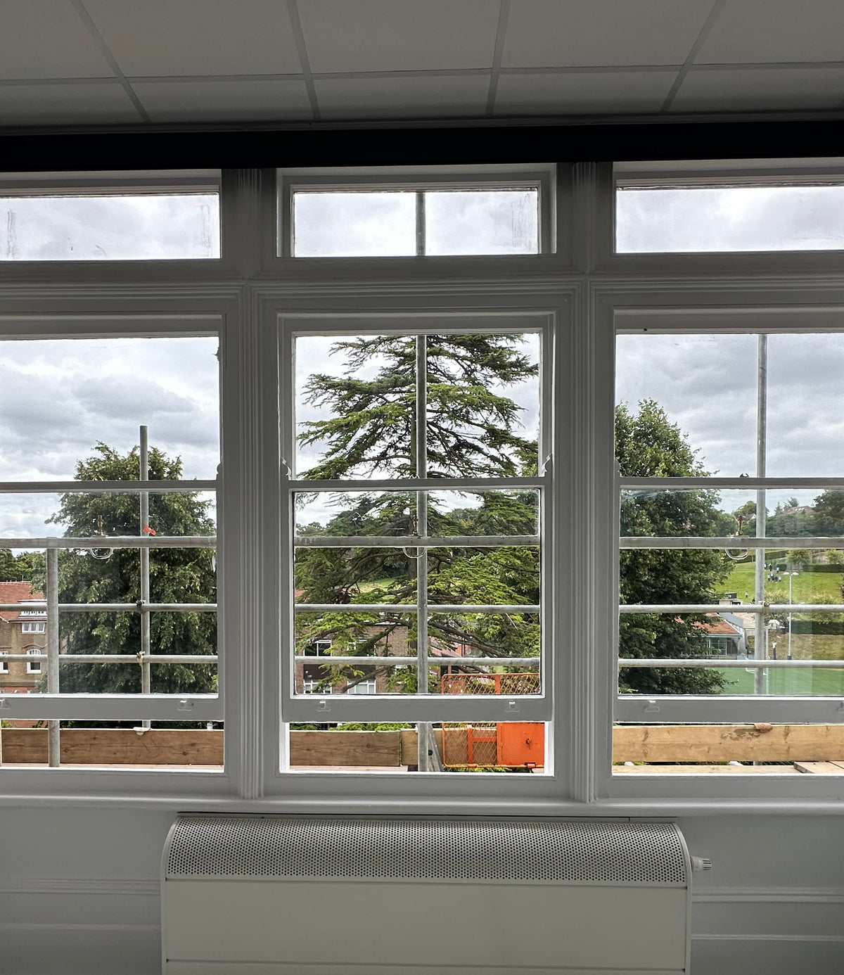 An internal view of a window looking out over trees and houses, with clear safety window film applied to the glass.