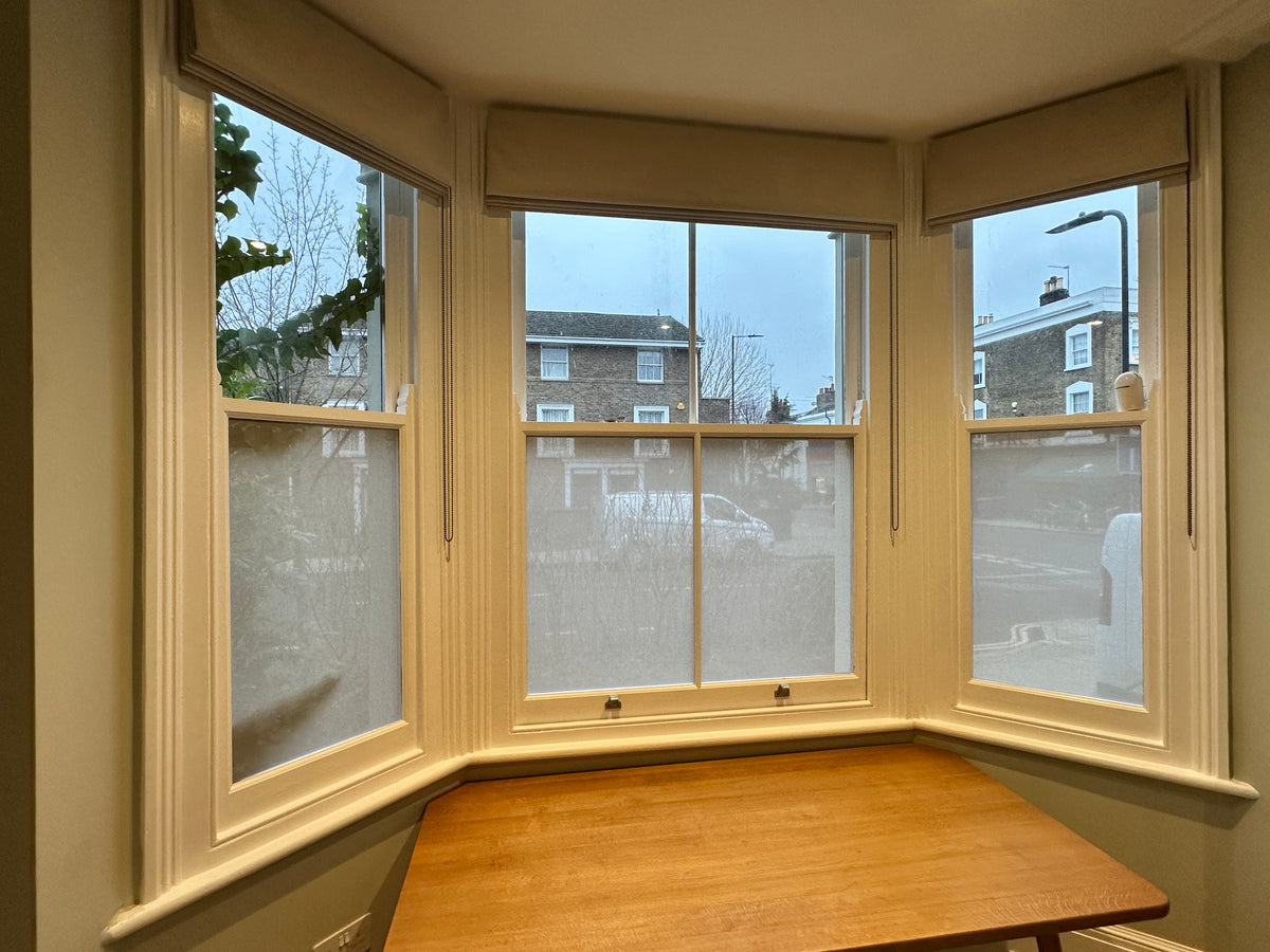 An internal view of a bay window with a fabric privacy window film applied to the lower panes.
