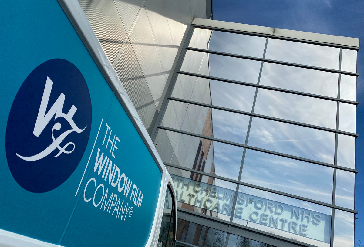 A van from The Window Film Company parked outside a large building with glass frontage