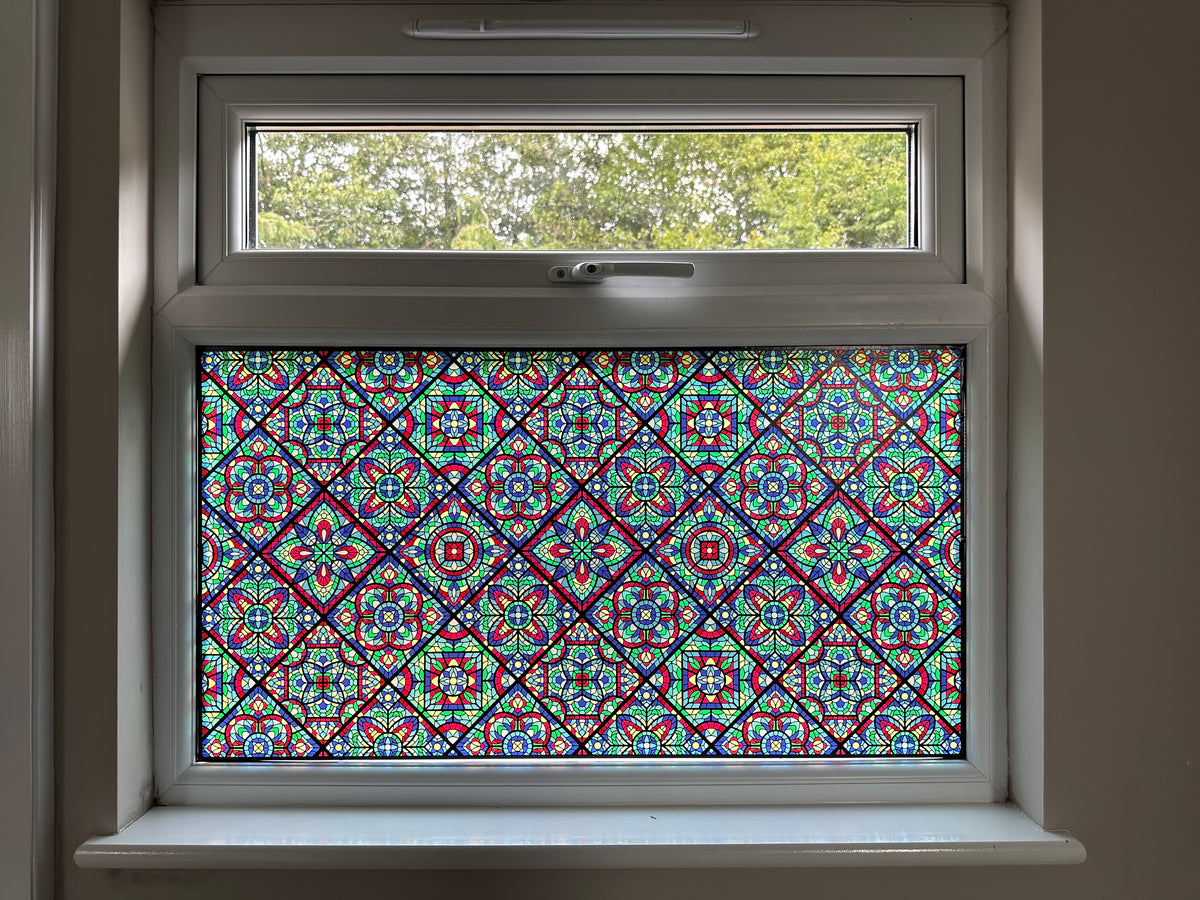 A colourful stained glass window film applied to the lower pane in a residential property. The pattern is a repeated design, featuring blue, green and red. 