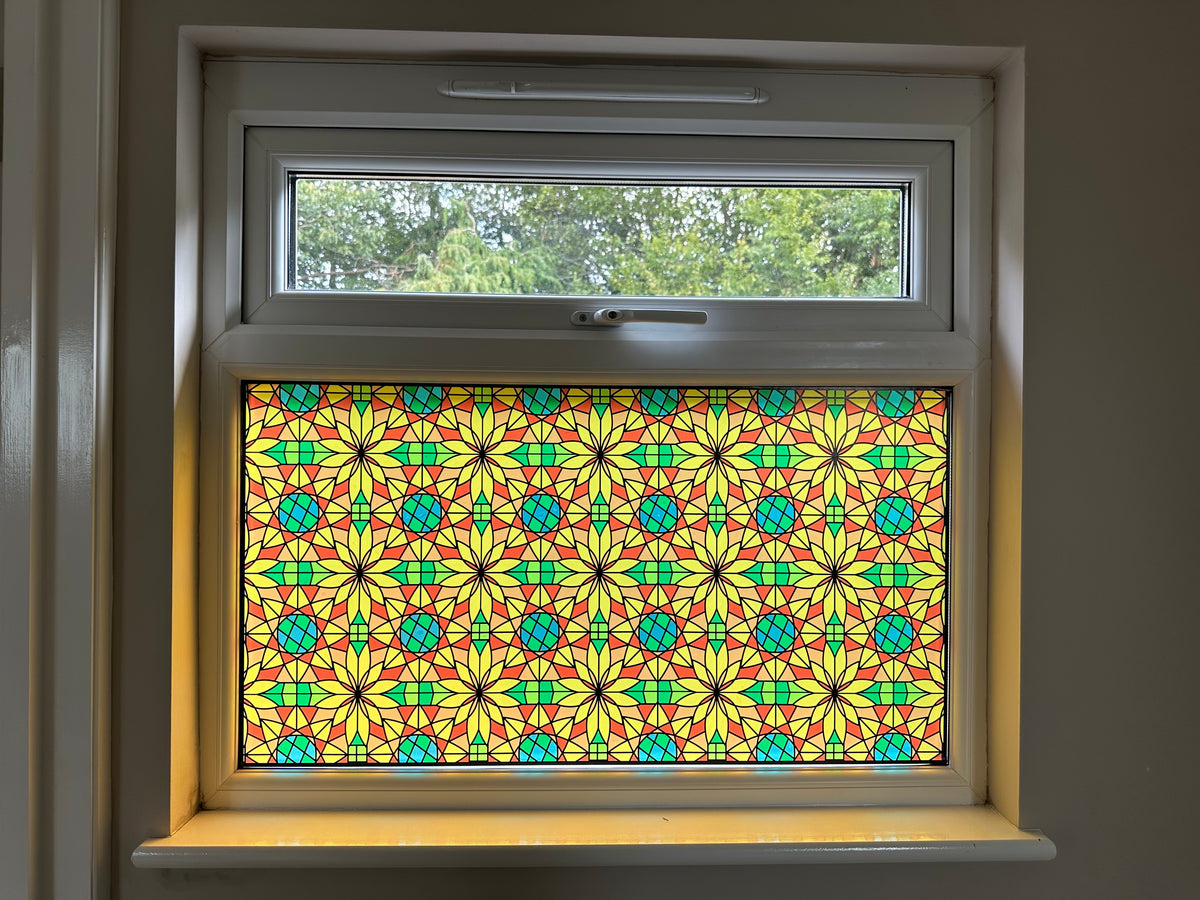 A colourful stained glass window panel with a repeating geometric pattern in yellow, green, and red, installed in a window for decor and privacy.