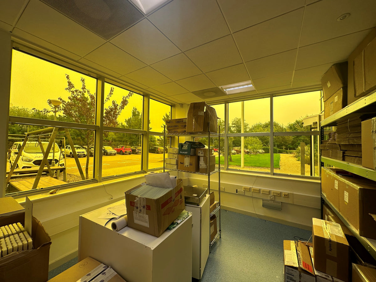 Storage room with shelves and boxes and Amber 81 UV protection window film applied to the large windows, allowing a view to a carpark outside. 