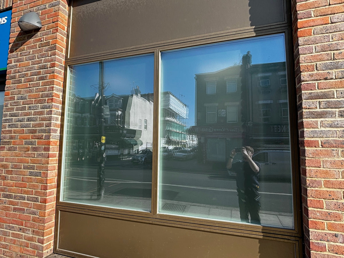 Large glass window, set into a brick building, with anti-graffiti window film applied to the glazing. 