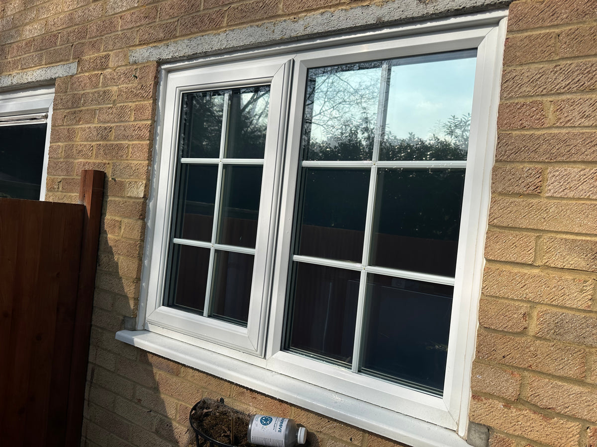 Window with white frame set into a brick wall in a residential setting; the glazing has had anti-graffiti window film applied. 