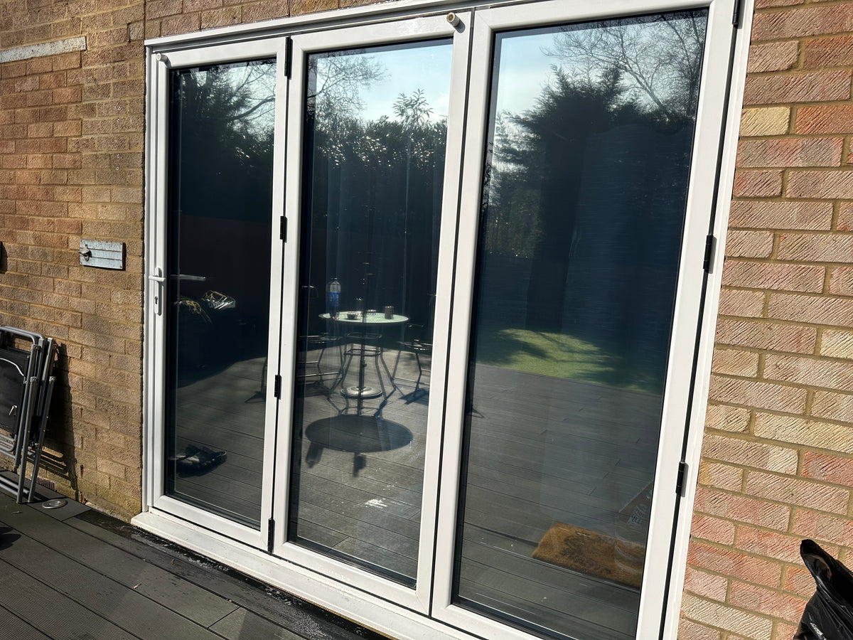 Exterior view of bifold doors with white frames and anti-graffiti window film applied to the glass. 