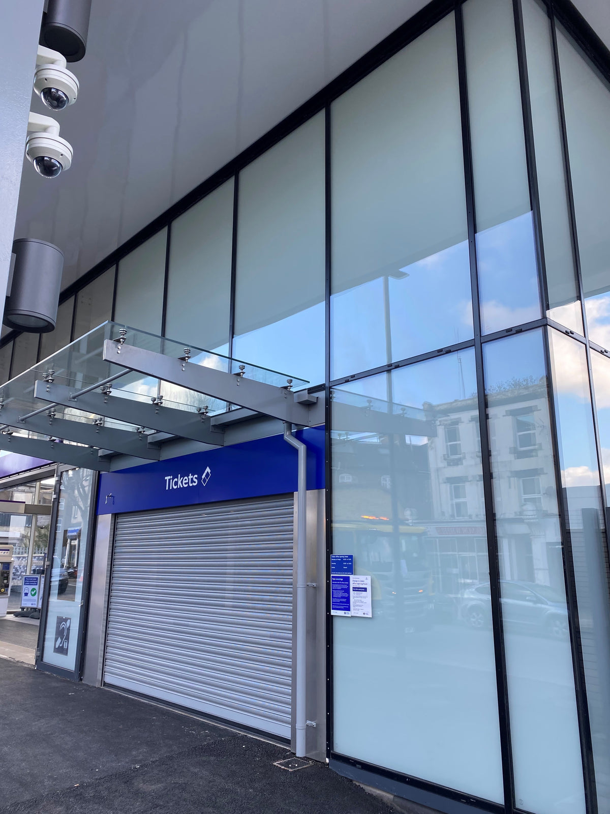 Closed ticket office with glass facade and blue sign on the building exterior, anti-graffiti window film has been applied to the glazing. 