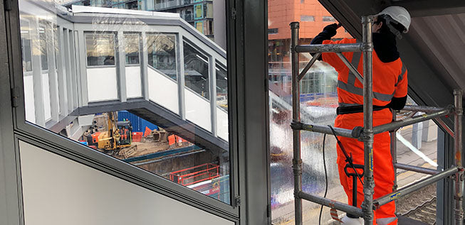 An installation expert fitting anti graffiti window film to the glazing throughout a rail station in the UK.