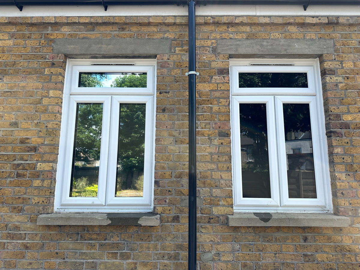 An external view of two windows set into a brick wall, with blackout privacy window film applied to all the panes within the windows.