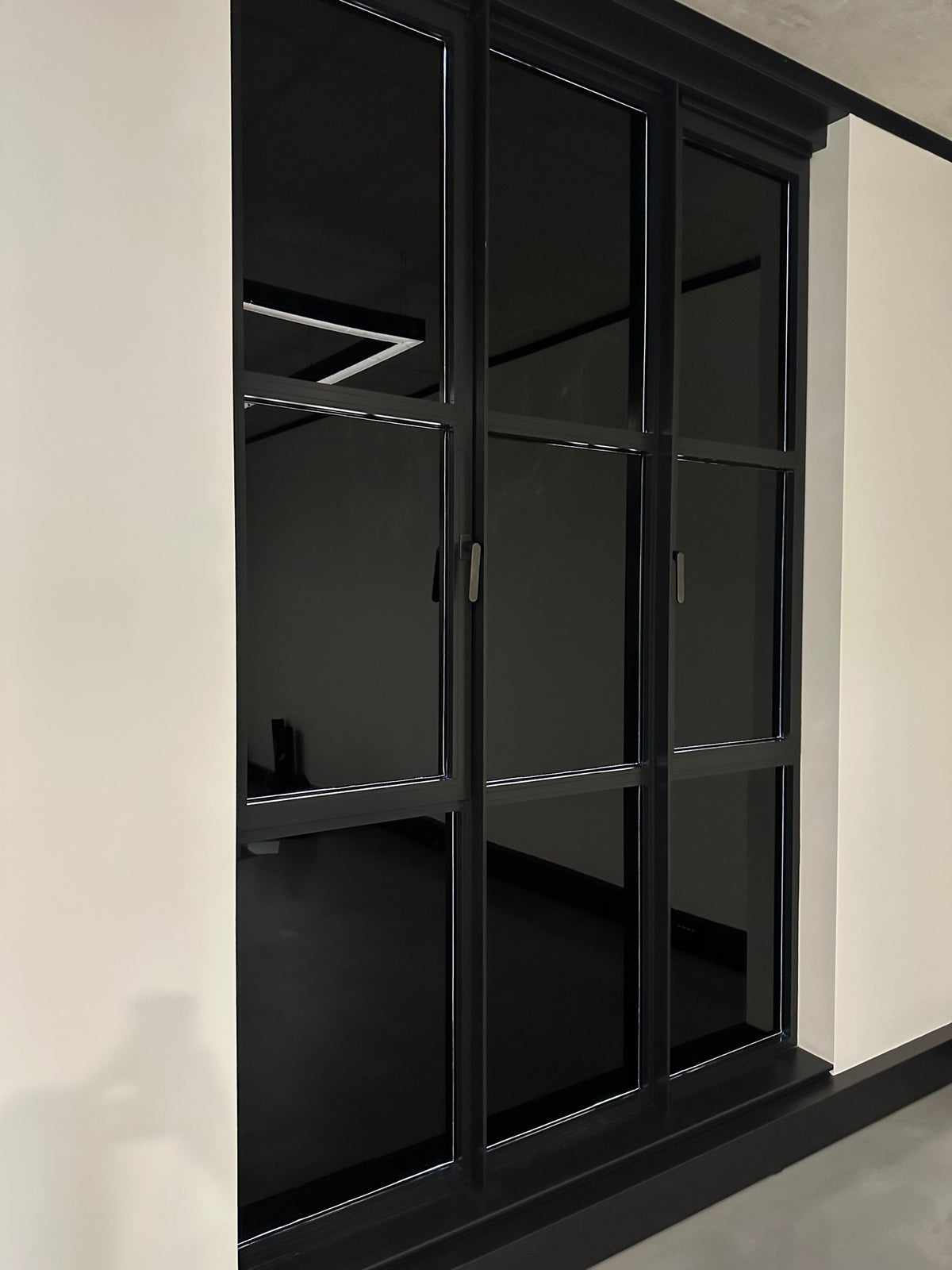 An internal view of a window split into nine panes, with blackout privacy film applied to each pane, transforming the glass to take on a solid black appearance.