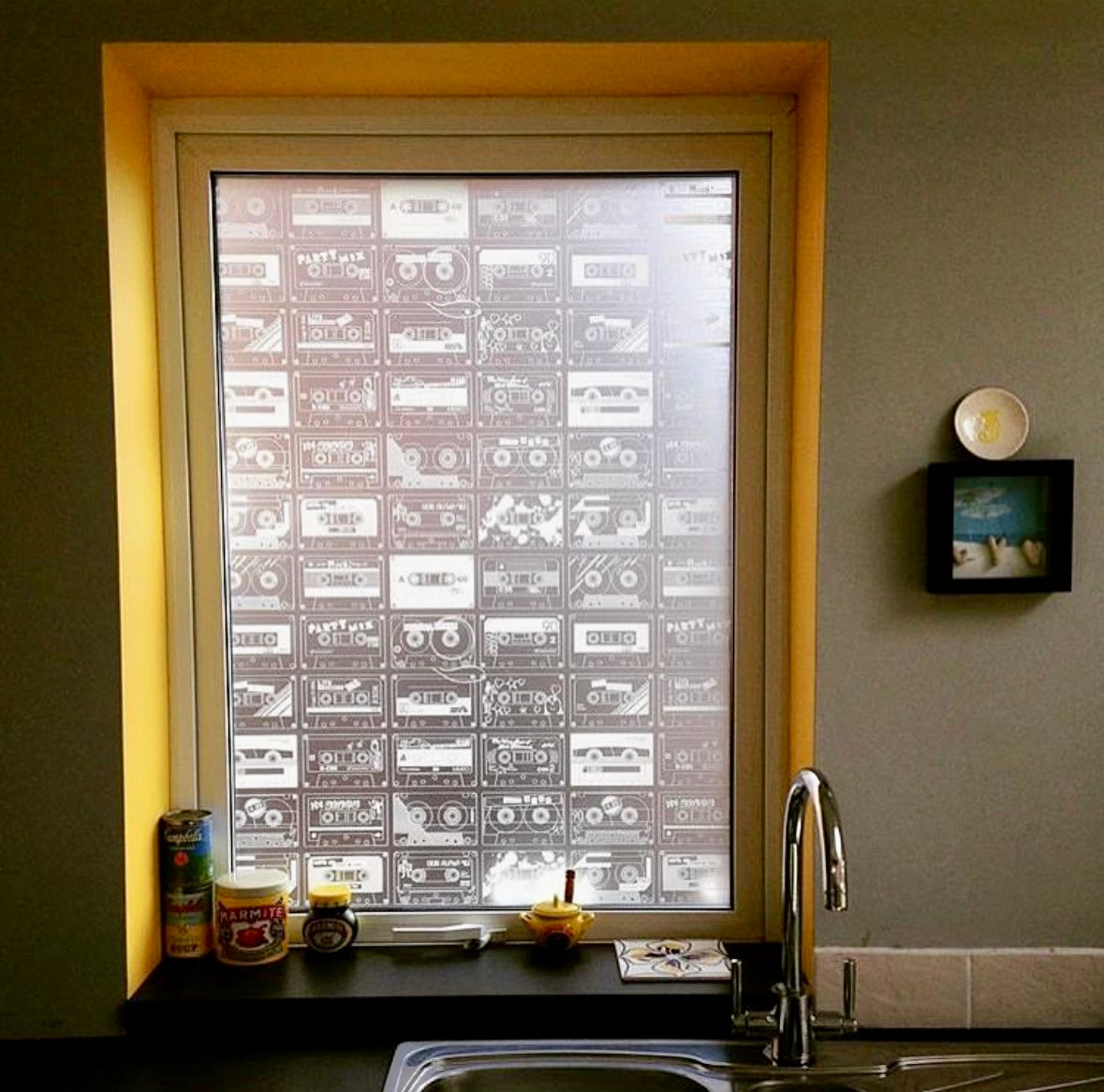 Window with retro cassette tape design window film, kitchen counter with items, and wall decor.