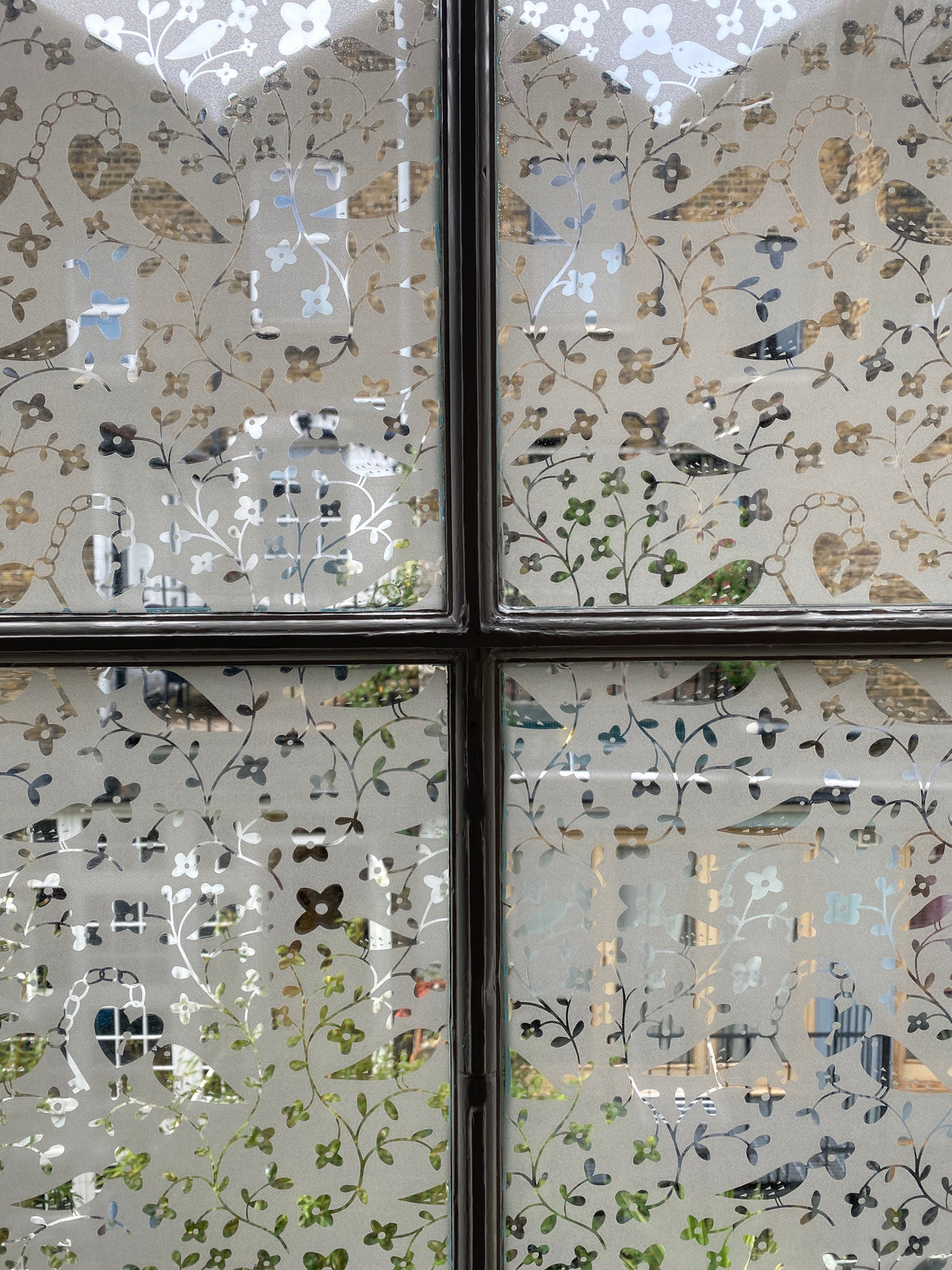 A window split into four panes looking out over neighbouring houses, with Rob Ryan clear on frost window film applied to the glass
