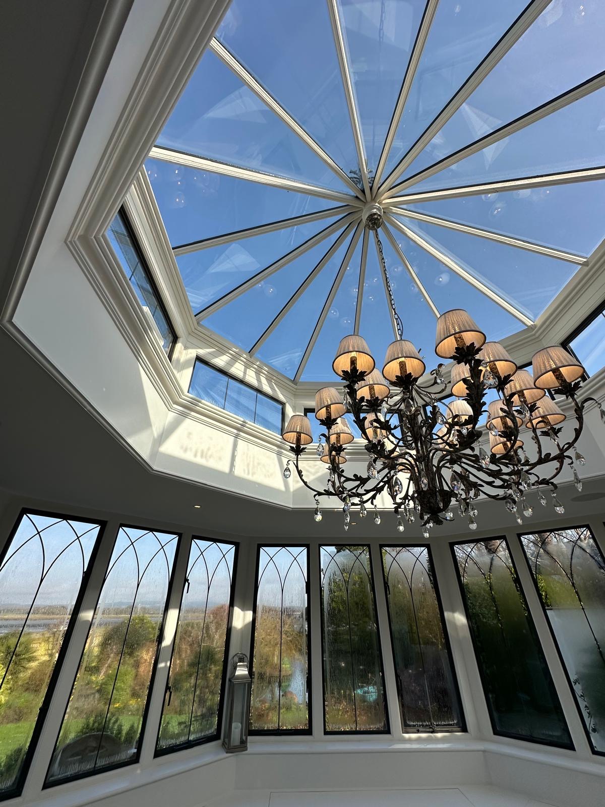 Orangery with a large rooflight split into multiple panes; each pane has solar control window film applied, there is also a chandelier hanging from the ceiling and large windows overlooking trees