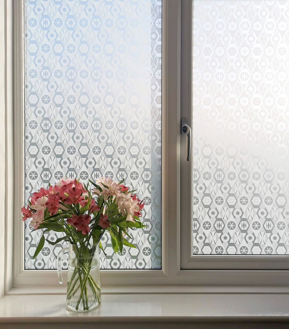 Window with two panes, both featuring Kate Farley window film. The film is a frosted effect and is delivering privacy, while there is a vase of flowers on the window ledge.