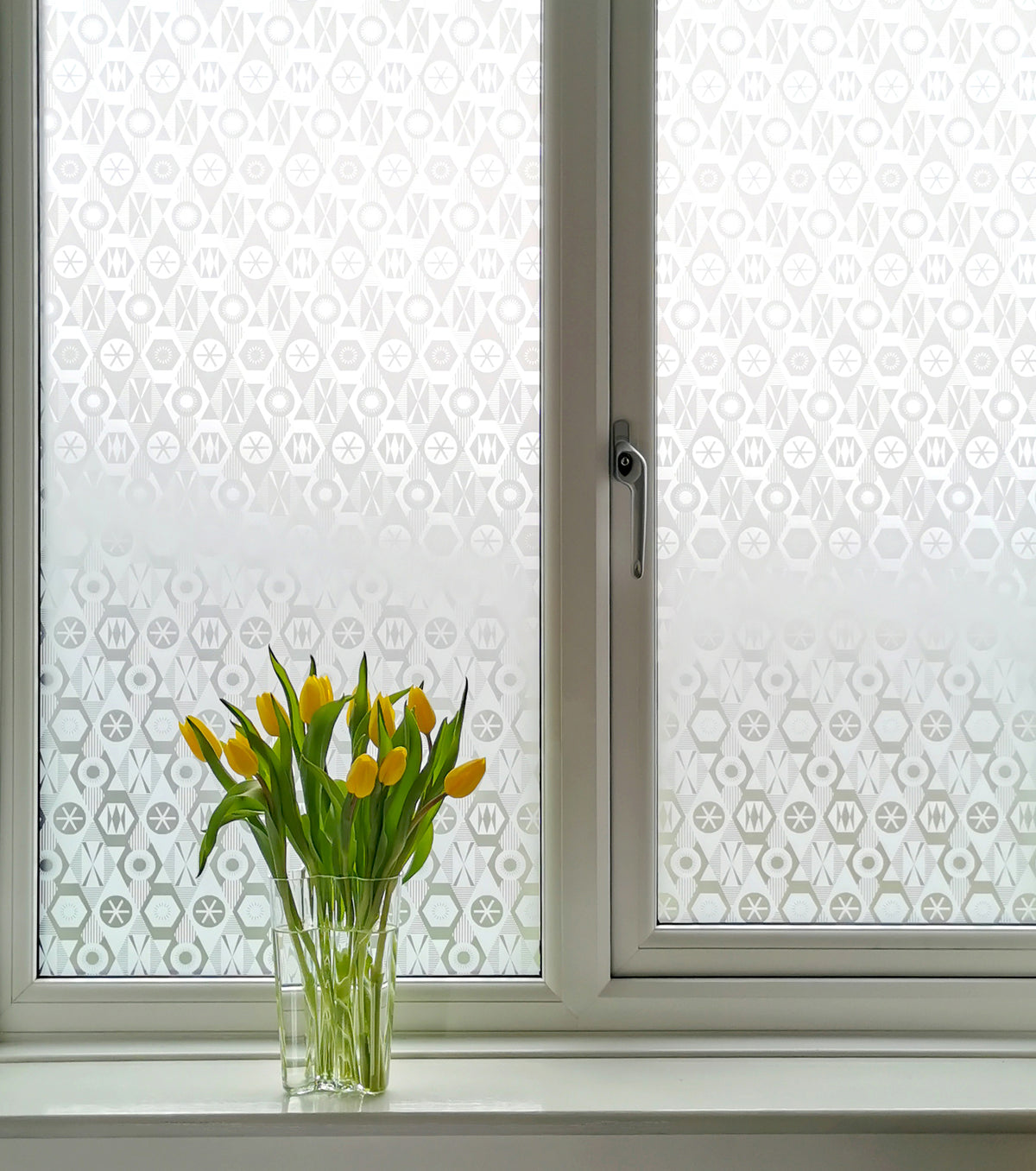 Window with decorative frosted window film and a vase of yellow tulips on a windowsill