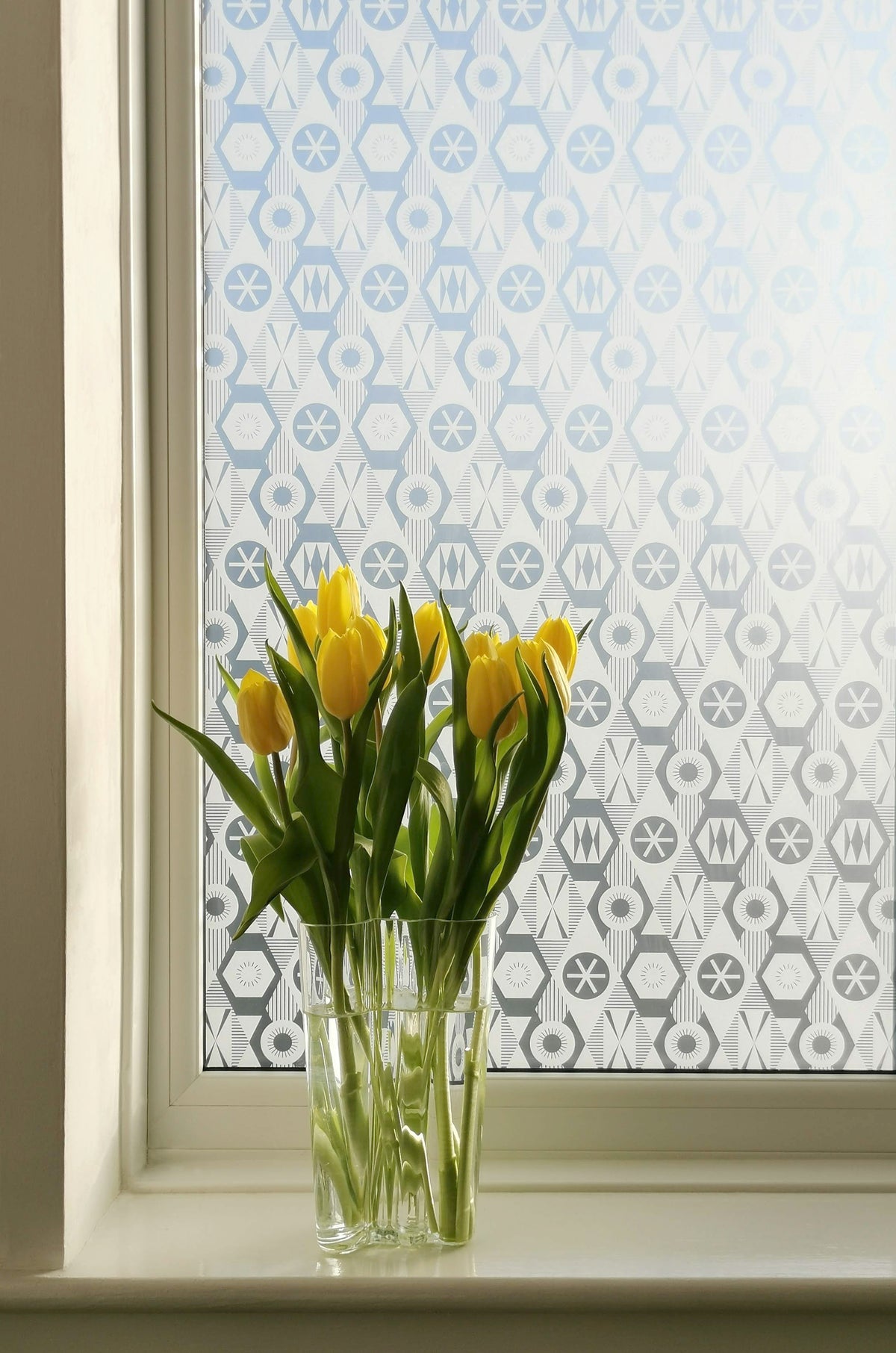 Diamonds inspired printed window film on a window with a bunch of flowers in a vase in the foreground.  