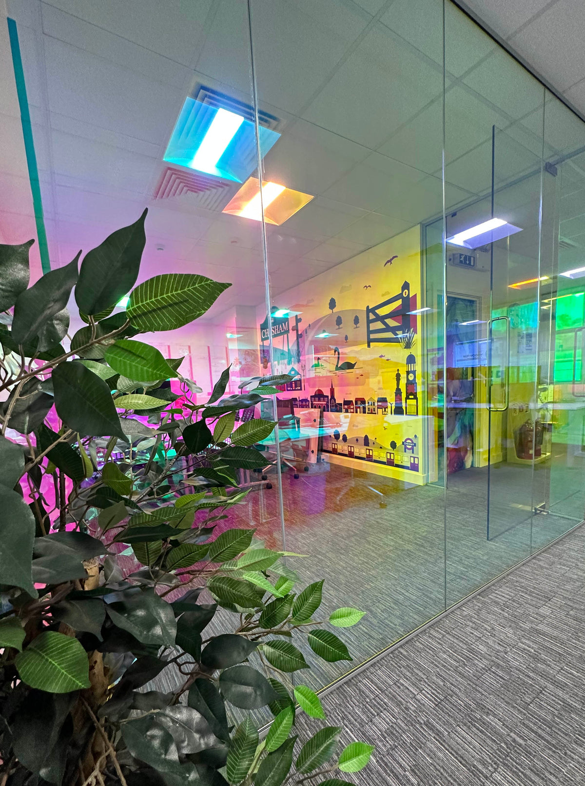 A view of a glass partition in a modern office, with dichroic window film applied to the glazing, giving the glass a colour-change effect.