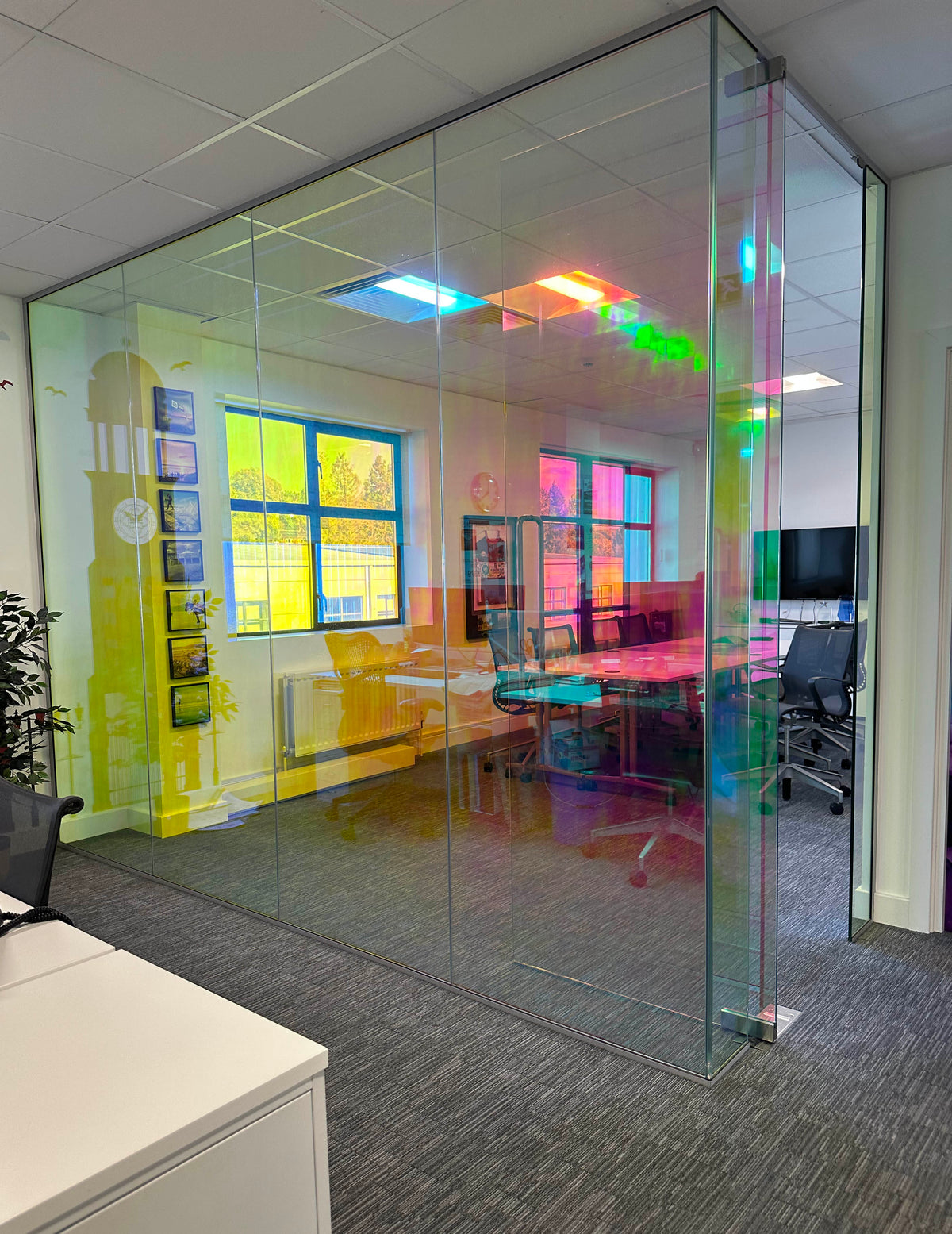 A large glass partition in a modern office, with dichroic window film applied to the glass. The film gives the glazing a colour-change effect, mimicking the appearance of dichroic glass.