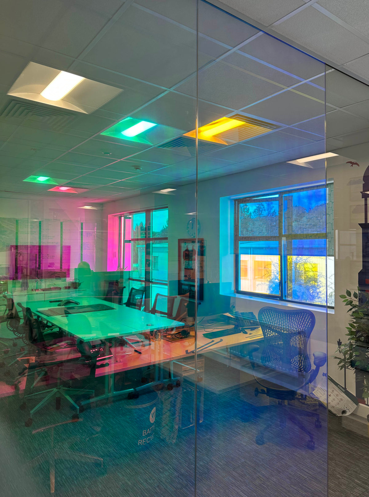 A view of a large glass partition in an office, with dichroic window film applied to the glass, delivering a shimmering, colour-change effect without the need for expensive replacement glass.