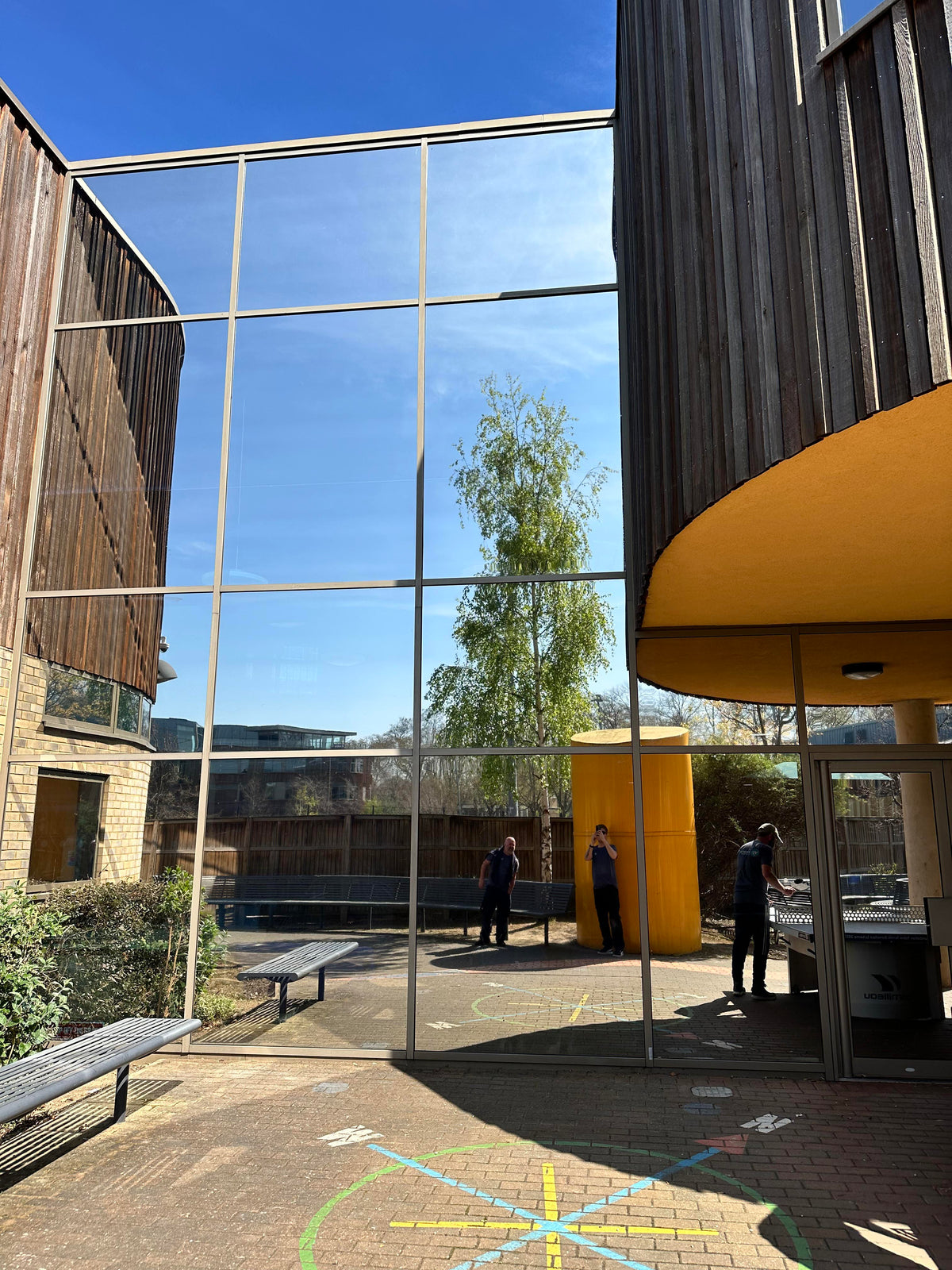 External view of a modern building with large glass windows. Each pane has reflective solar control window film applied to it, giving a silver, mirrored appearance. 