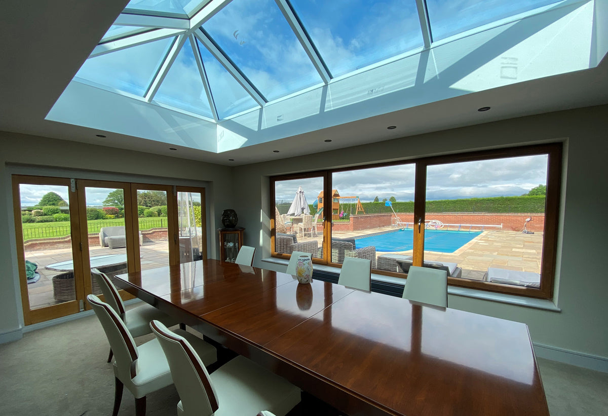 Modern dining room with large windows and a skylight overlooking a garden and pool. The windows have been protected with a UV window film.