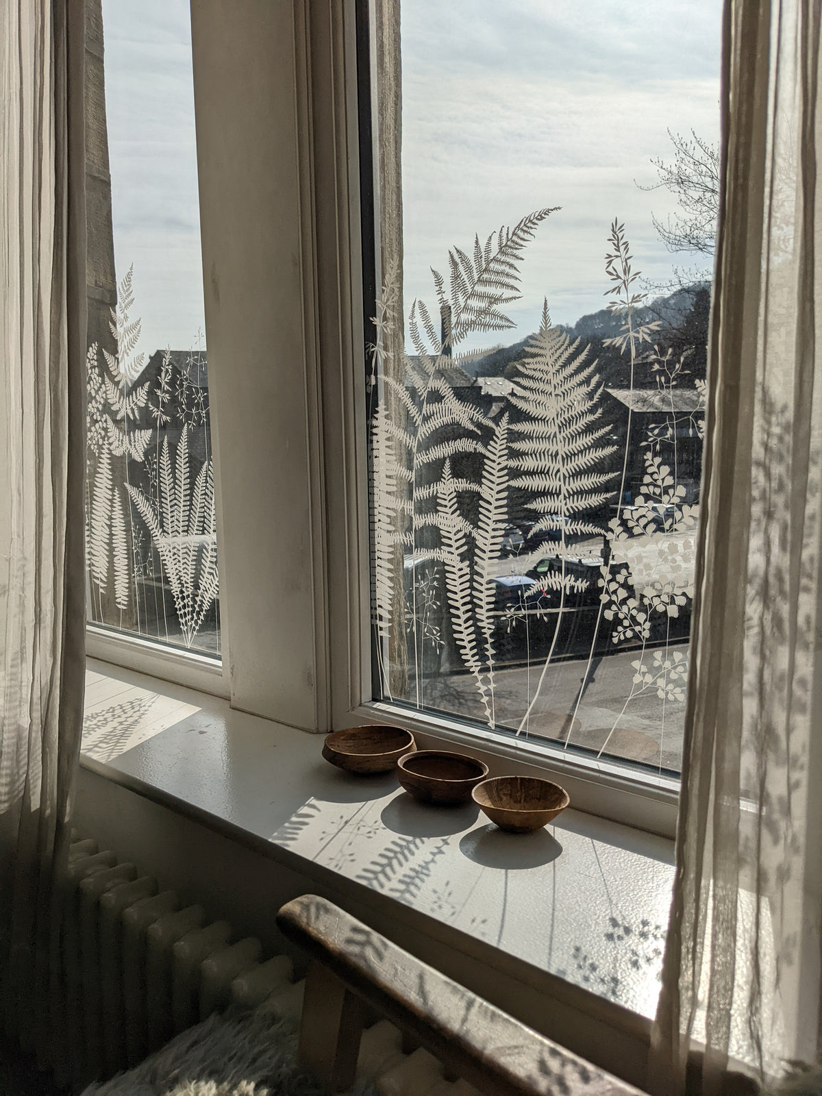 Window with decorative frost patterns, small bowls on a windowsill, and sheer curtains.