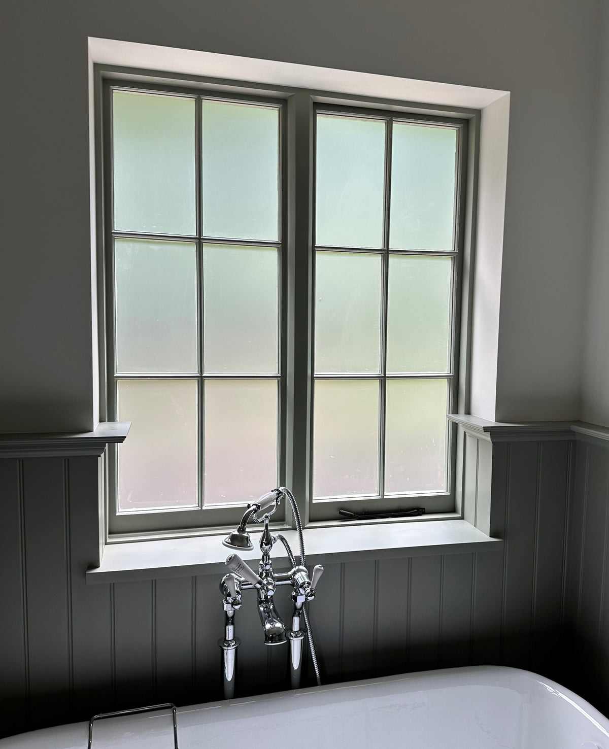 Bathroom with a window, that has frosted window film applied for privacy, above a bathtub and shower fixtures.