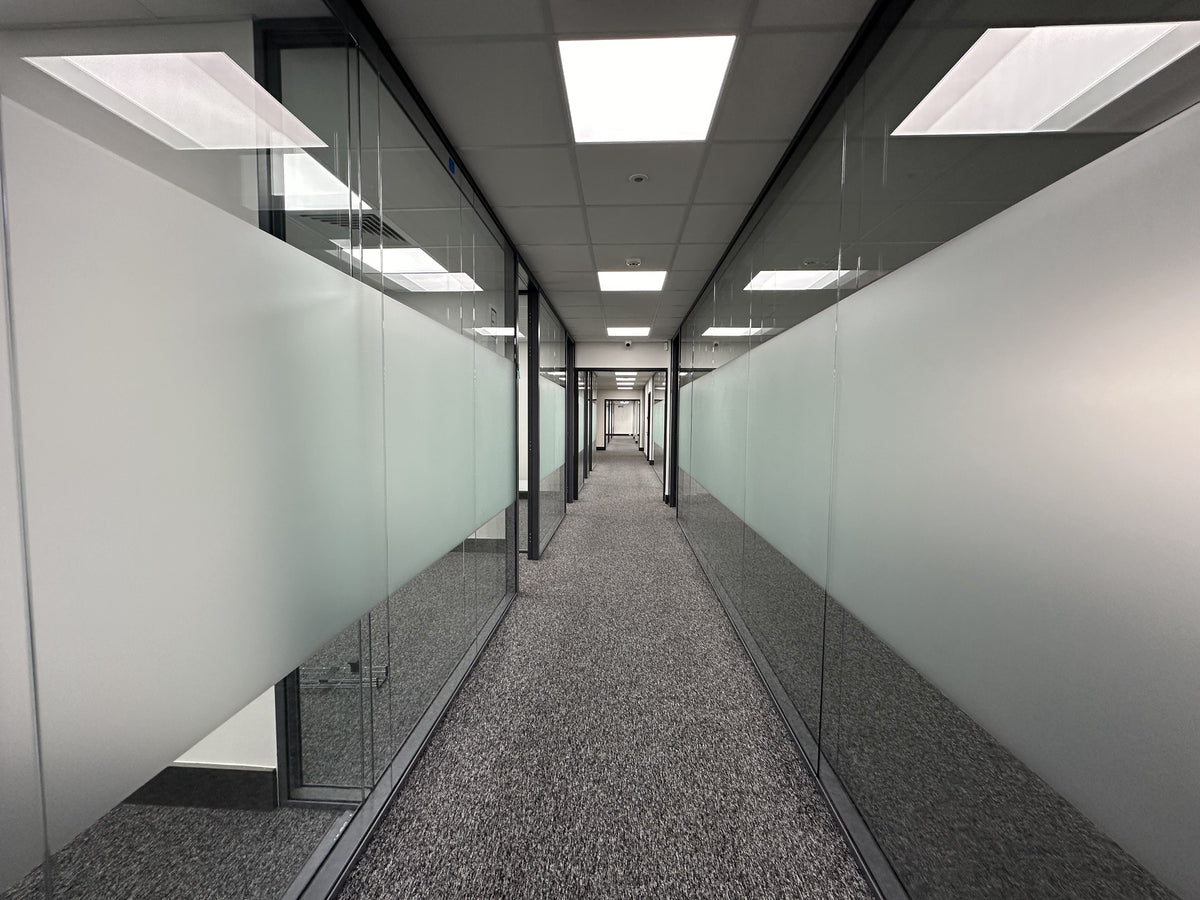 Long corridor with glass offices either side which has a band of frosted window film applied.