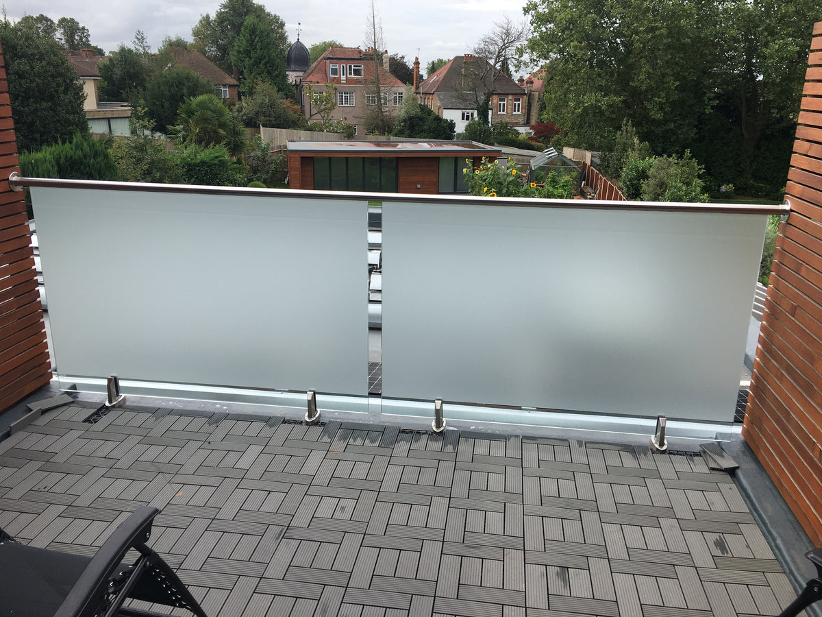 Glass balustrade with Frostbrite frosted window film applied, on a balcony with a view of residential houses and trees.