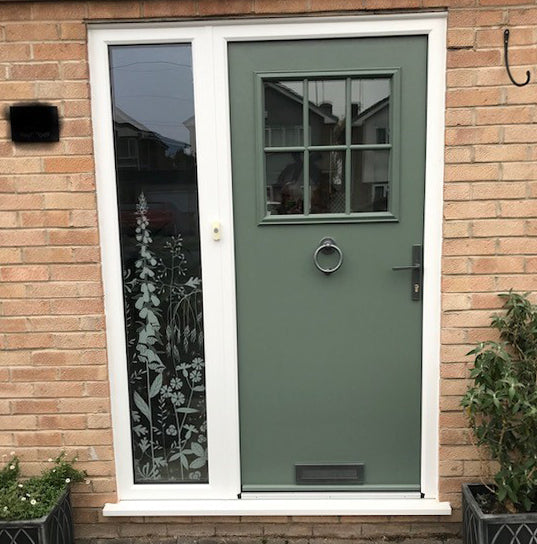 External view of a home with a green front door and a Hannah Nunn window film applied to a tall thin window to the left of the door.