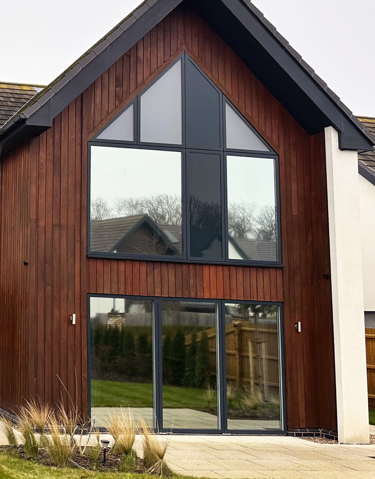 A modern house with a wooden facade and large glass windows, with reflective solar control window film applied to them.