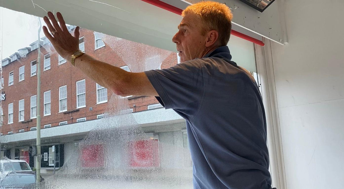 A window film installer fitting clear safety and security window film to a shop.