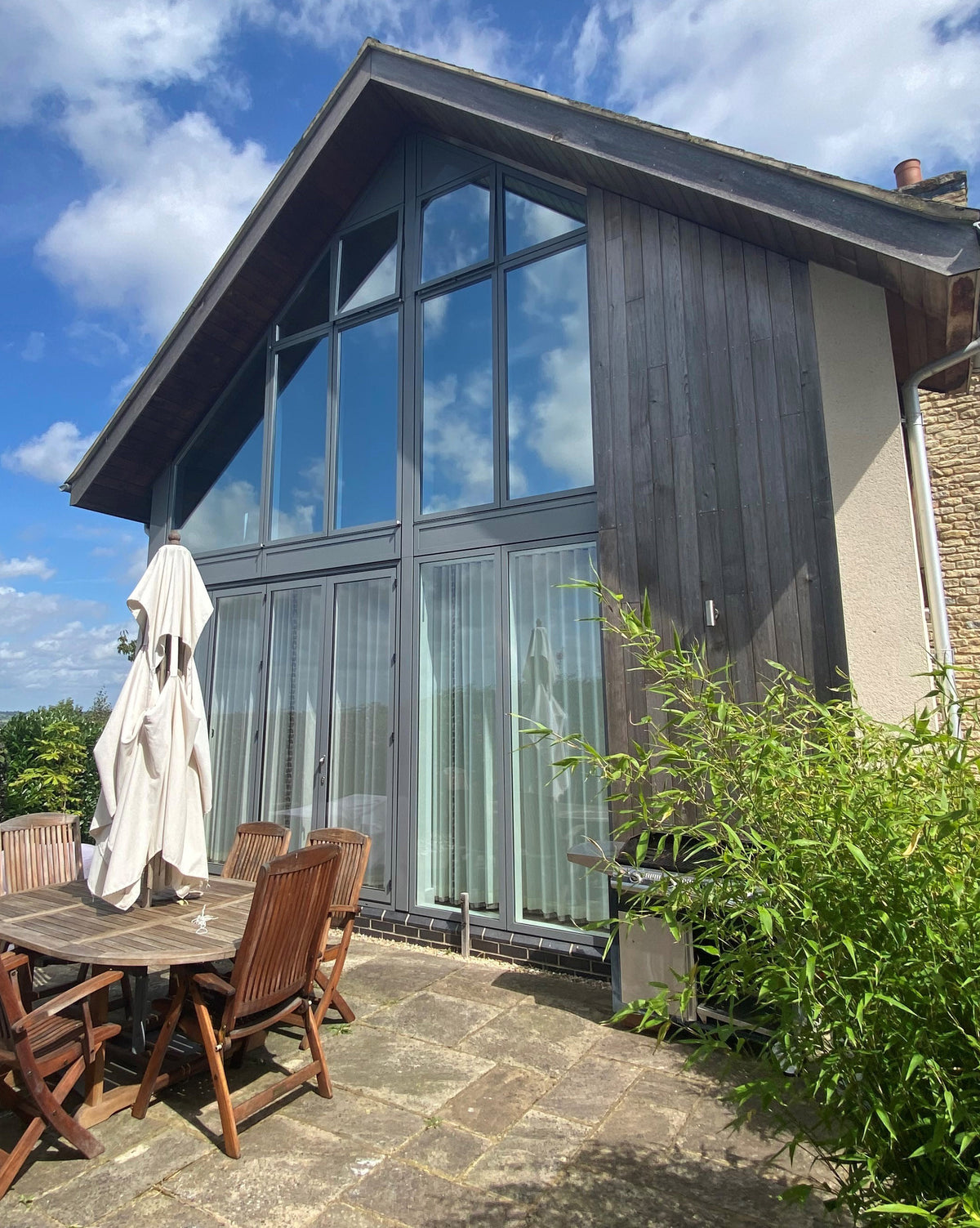 House exterior with large windows, outdoor furniture, and greenery under a blue sky. Heat and glare reducing window film has been applied to the internal face of the glass.