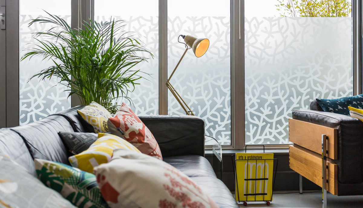Living room with a sofa, decorative pillows, and a plant in front of a window that has got a frosted pattern printed onto a frosted film.