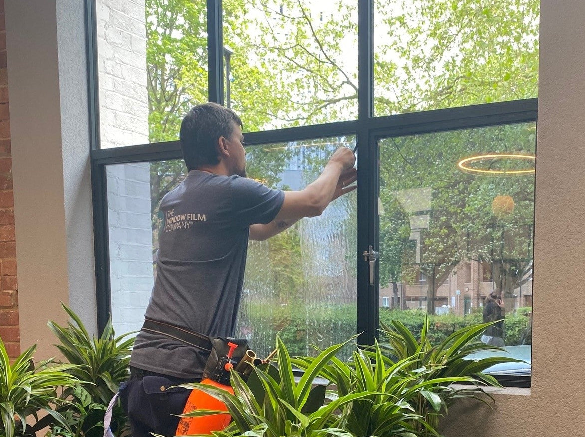 An installer from The Window Film Company installing Optiview window film to reduce heat and glare in an office.