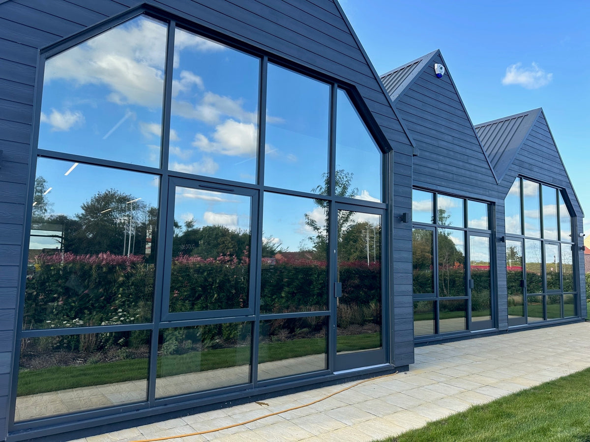 External view of a large Modern house with large glass windows with solar control window film applied, reflecting a blue sky and trees on a bright sunny day. 