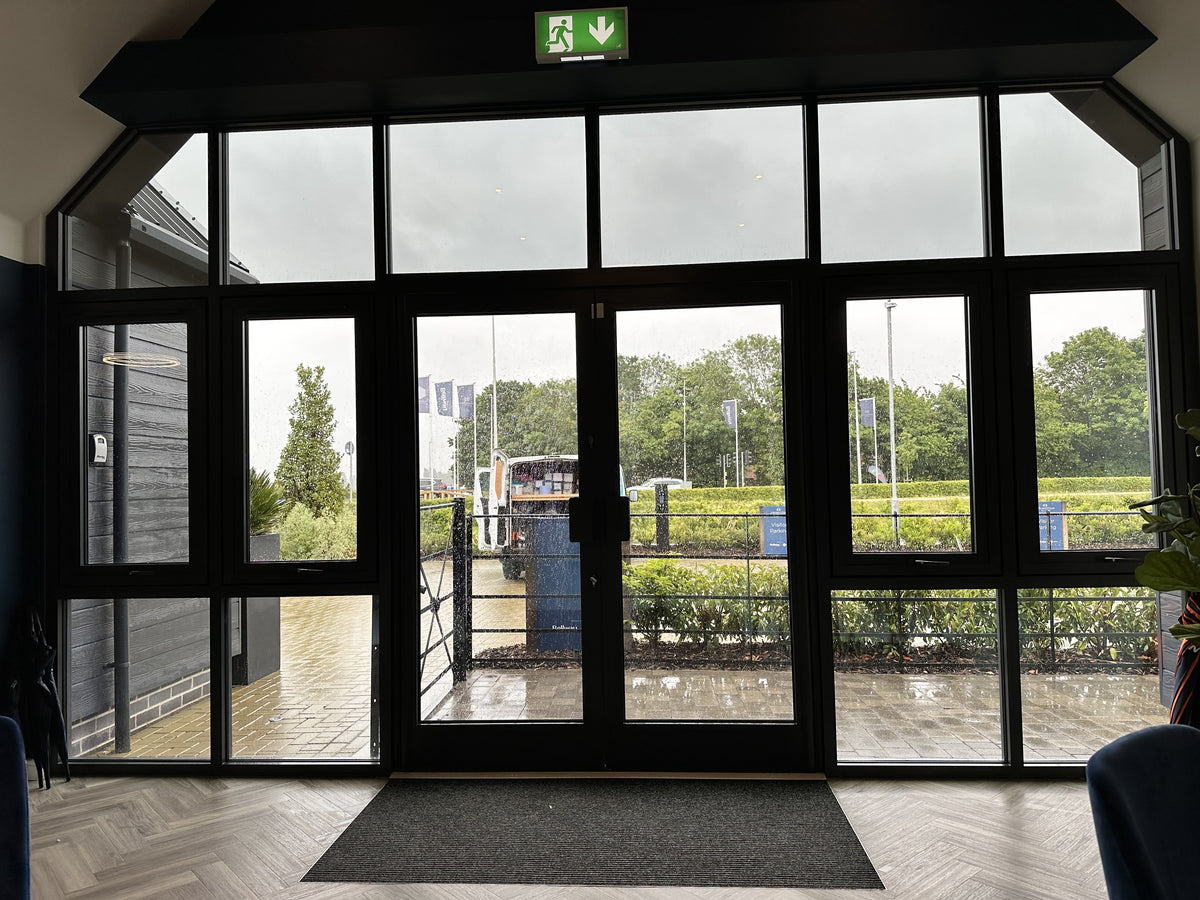 Large glass door with multiple panels, each with heat reduction window film applied to it,  leading to an outdoor area with trees and a carpark