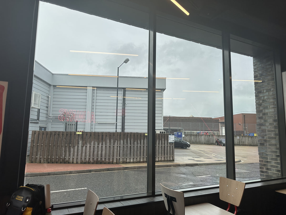 View from a window into an industrial area with a fence and buildings; the glazing has had heat and glare reduction window film applied to it. 