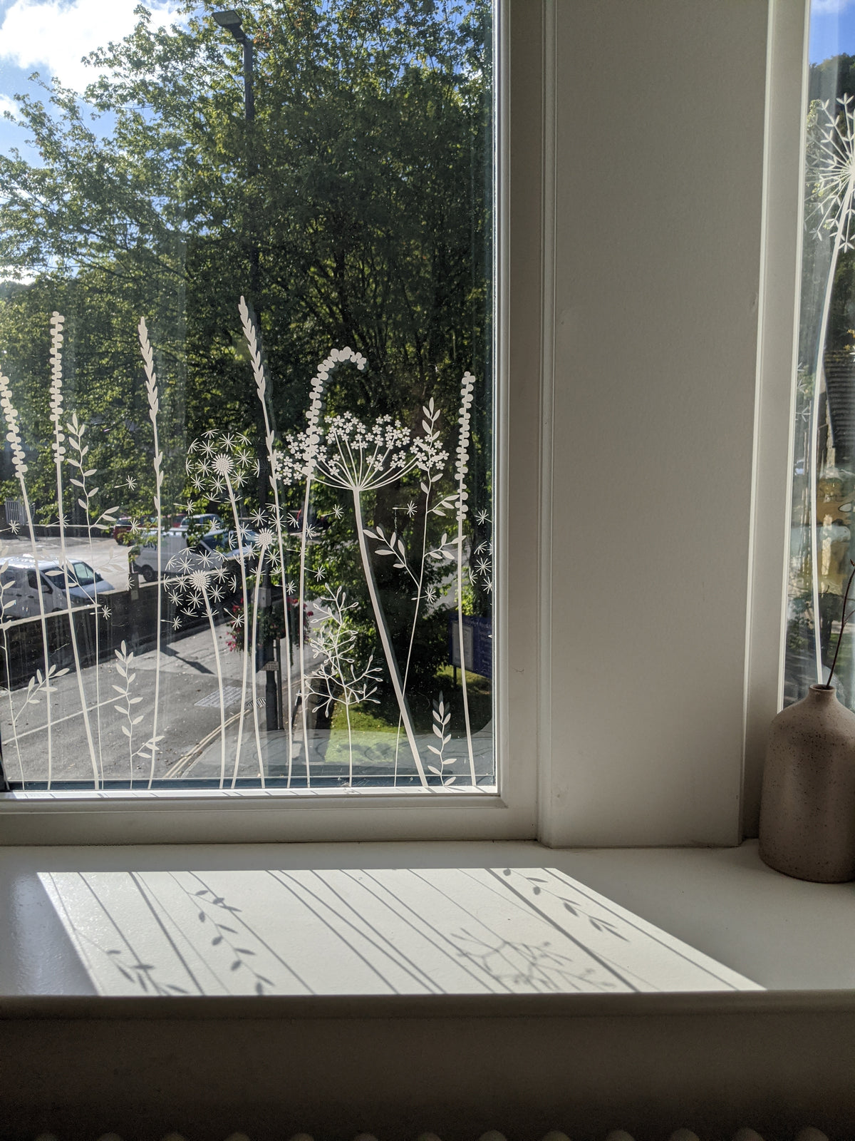 Window film with decorative plant pattern, view of street outside, and a vase on a windowsill.