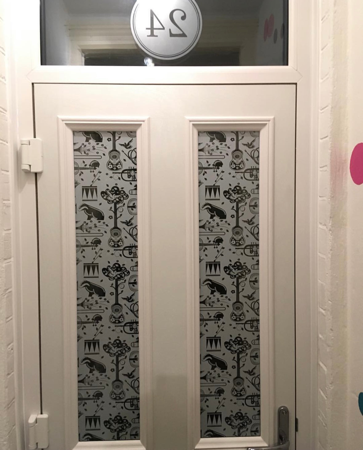 Decorative glass door with a patterned window film design in a room with white walls and a house number. 