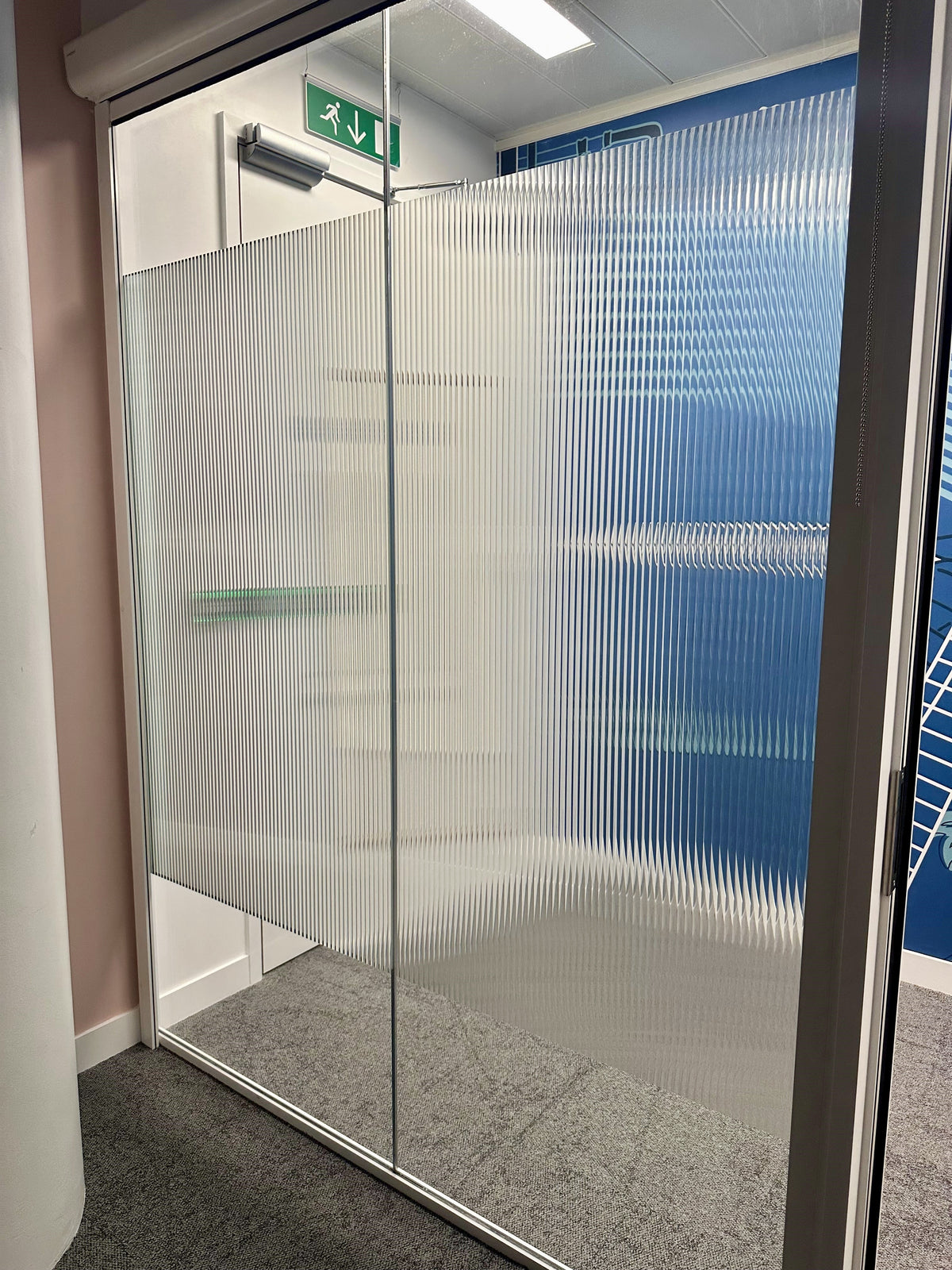 Evoke reeded window film applied to a lass partition as a band which leaves clear glass top and bottom.  The reeded glass effect looks very retro.