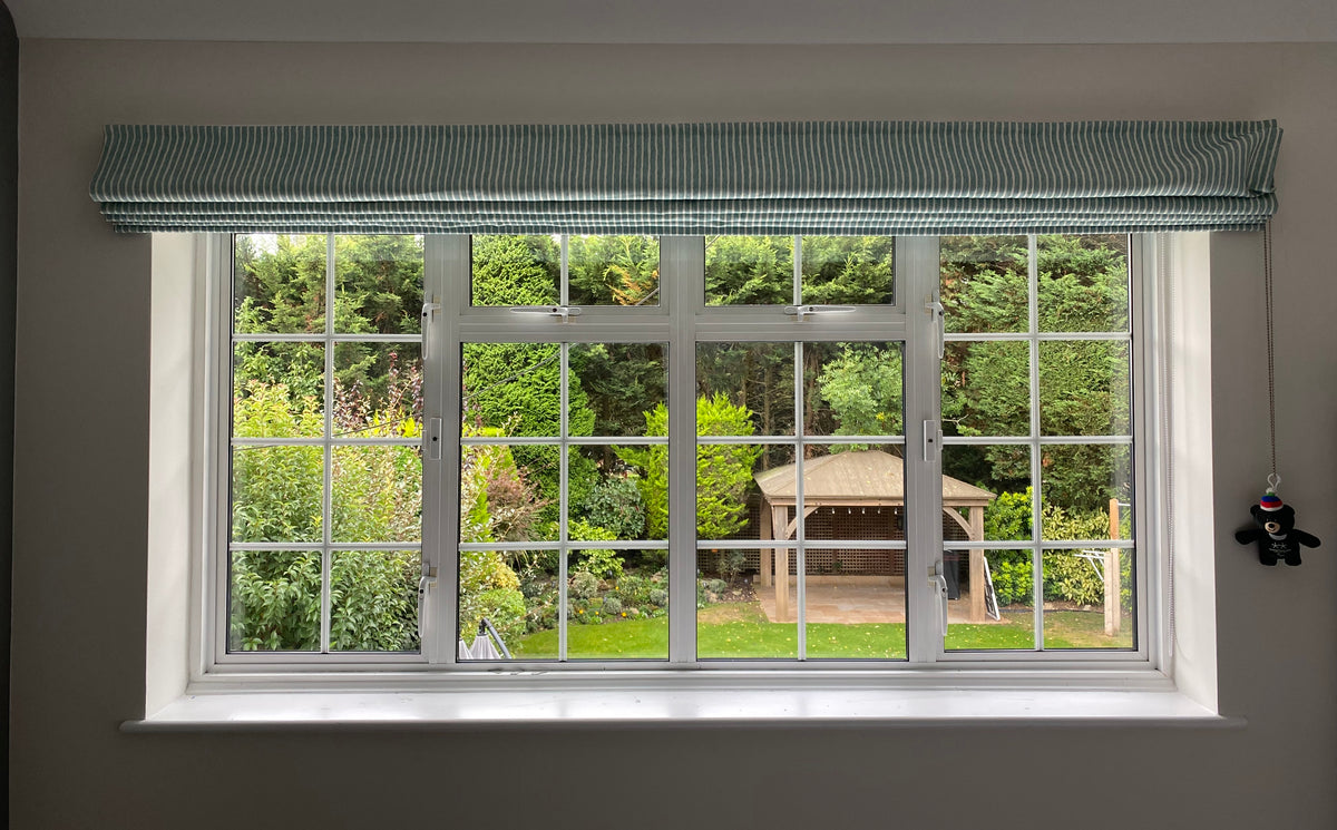 Window with green roller blind overlooking a garden with a gazebo. There is clear safety window film on the glass.