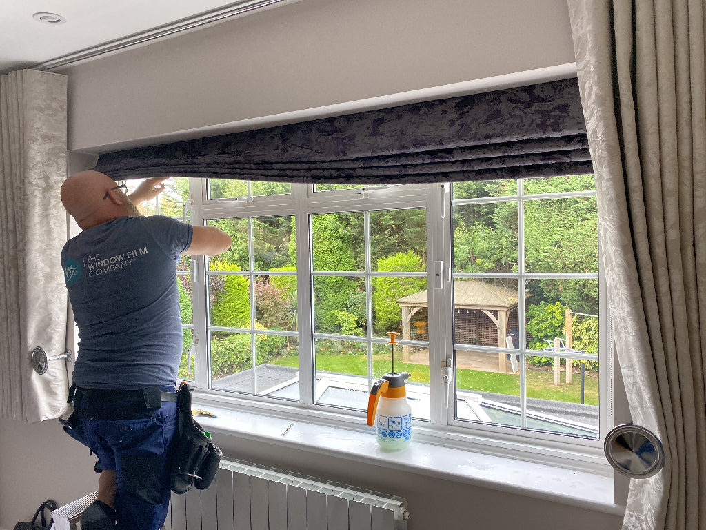 Person installing window film on a window with a view of greenery outside.