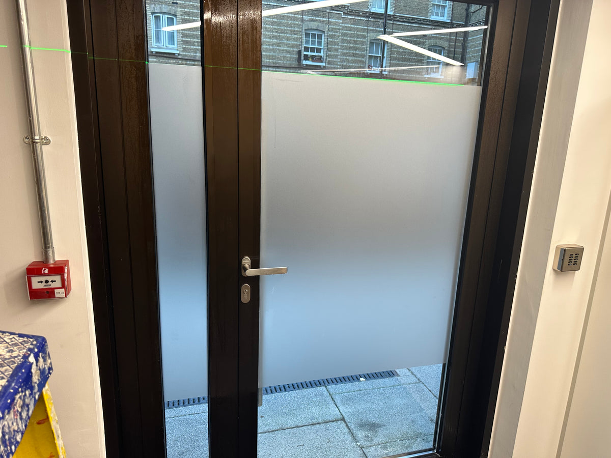 Glass door with wooden frame leading to an outdoor area, a band of frosted film has been applied to the central part of the glazing. 