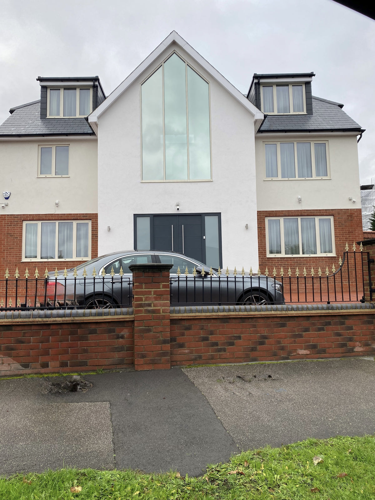 The outside view of a house which has a very large apex window above their front door.  This shaped window has had a mirrored window film applied to it for solar control.