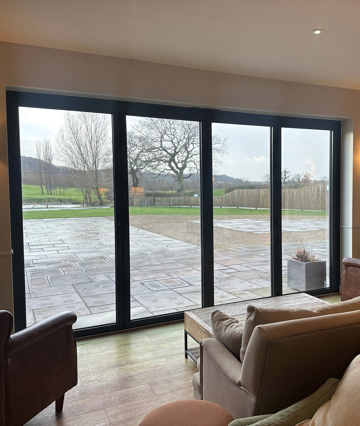 Living room with large glass doors with heat reduction window film applied, leading to a patio area with trees and a fence.