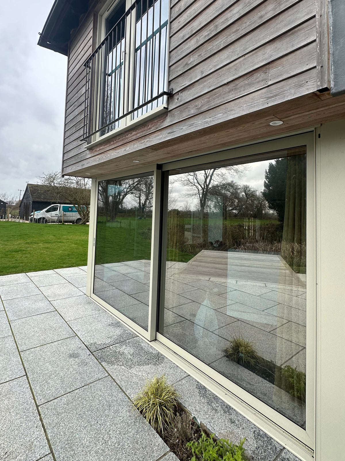 Modern house exterior with large glass windows and a paved patio area, heat reduction window film has been applied to the glazing. 