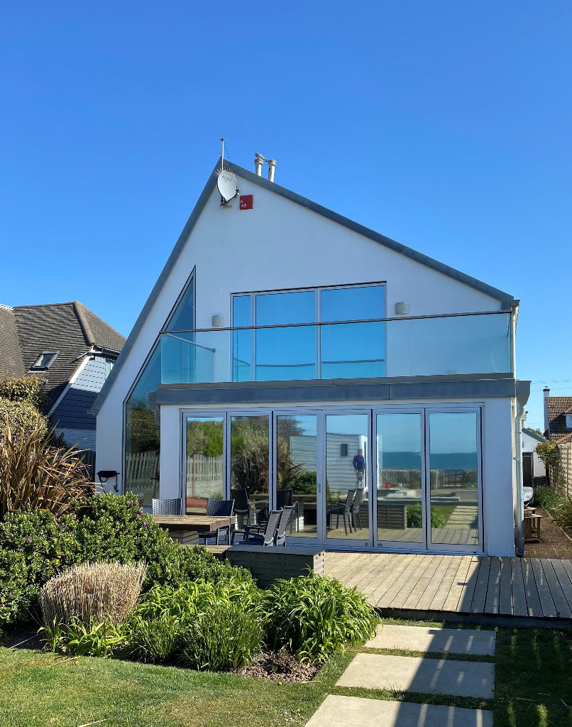 Mirrored window film for solar control applied to the large windows and patio doors of a modern house.