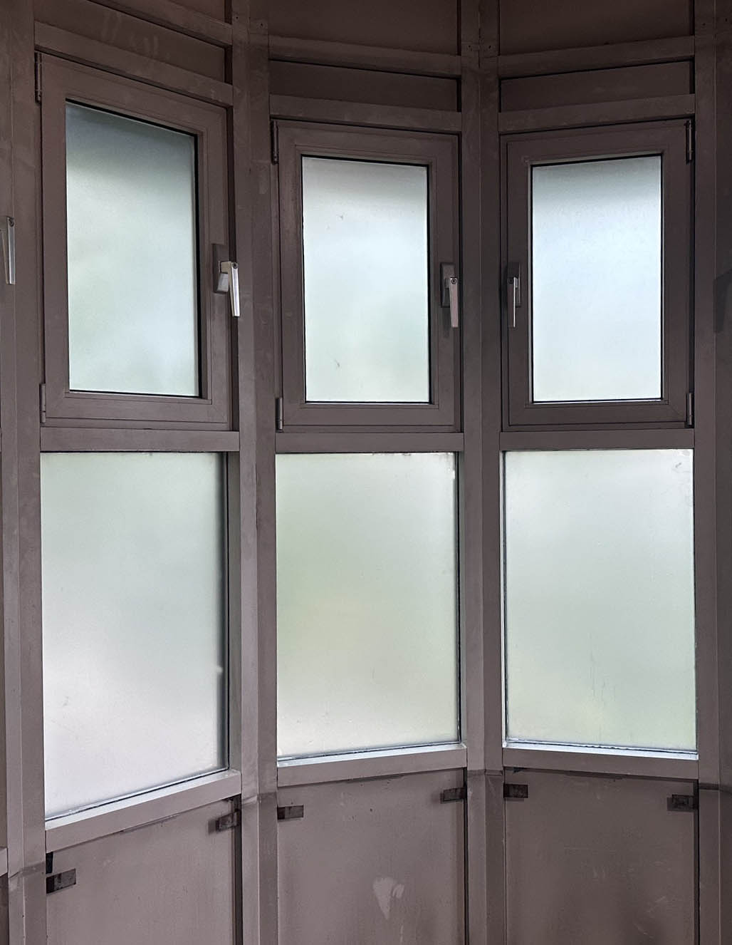 An internal view of a bank of six window panes with white frames. Each pane has frosted window film applied to provide two-way privacy.