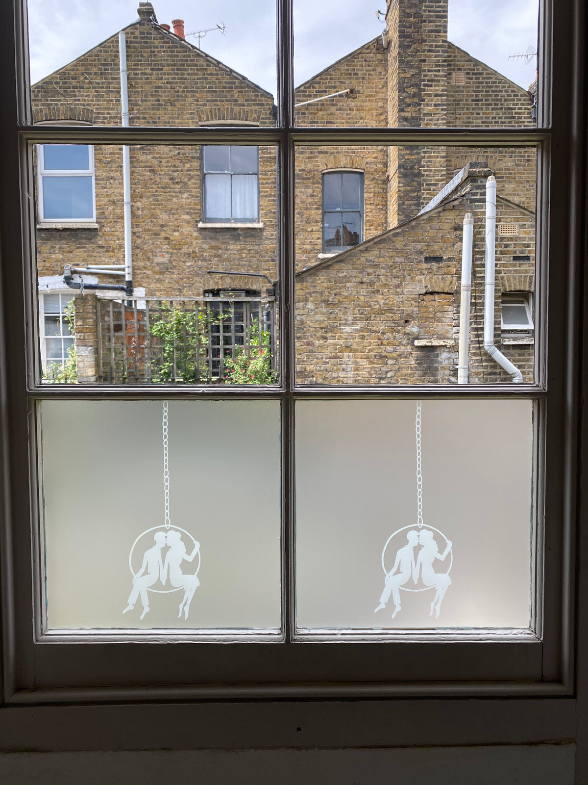Window split into six panes, looking out over neighbouring houses, Rob Ryan designer window film ahs been applied to the lower two panes. 